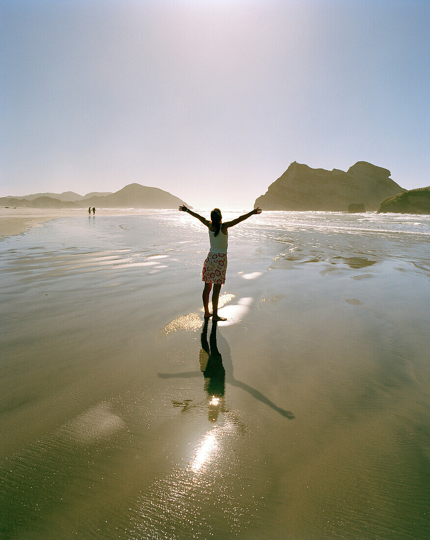 Woman standing in the shallow water at Wharariki Beach, northwest coast, South Island, New Zealand