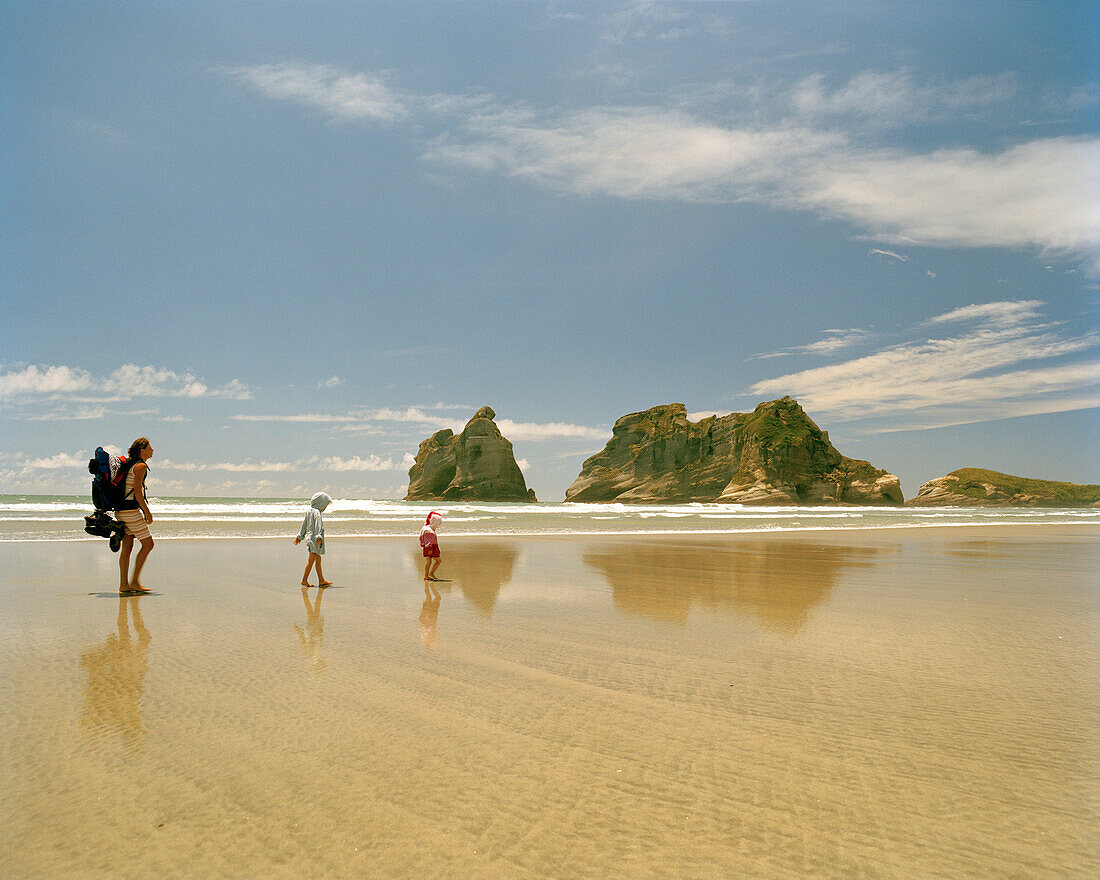 Frau und Kinder wandern durch seichtes Wasser, Wharariki Beach, Nordwestküste, Südinsel, Neuseeland