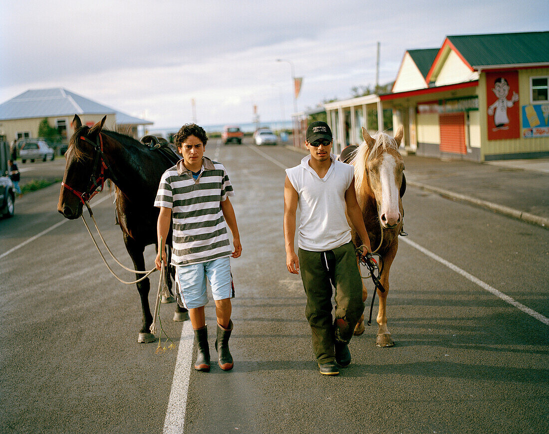 Zwei junge Maori Männer mit Pferden auf der Hauptstraße des Dorfes Te Araroa, Eastcape, Nordinsel, Neuseeland