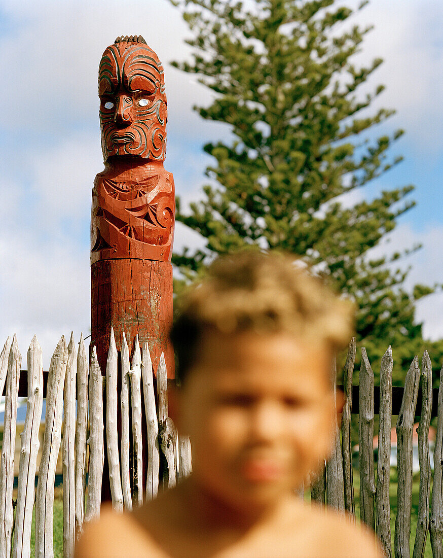 Ein Maori Junge und eine geschnitzte Figur am Schuleingang, Torere, Nordküste, Eastcape, Nordinsel, Neuseeland
