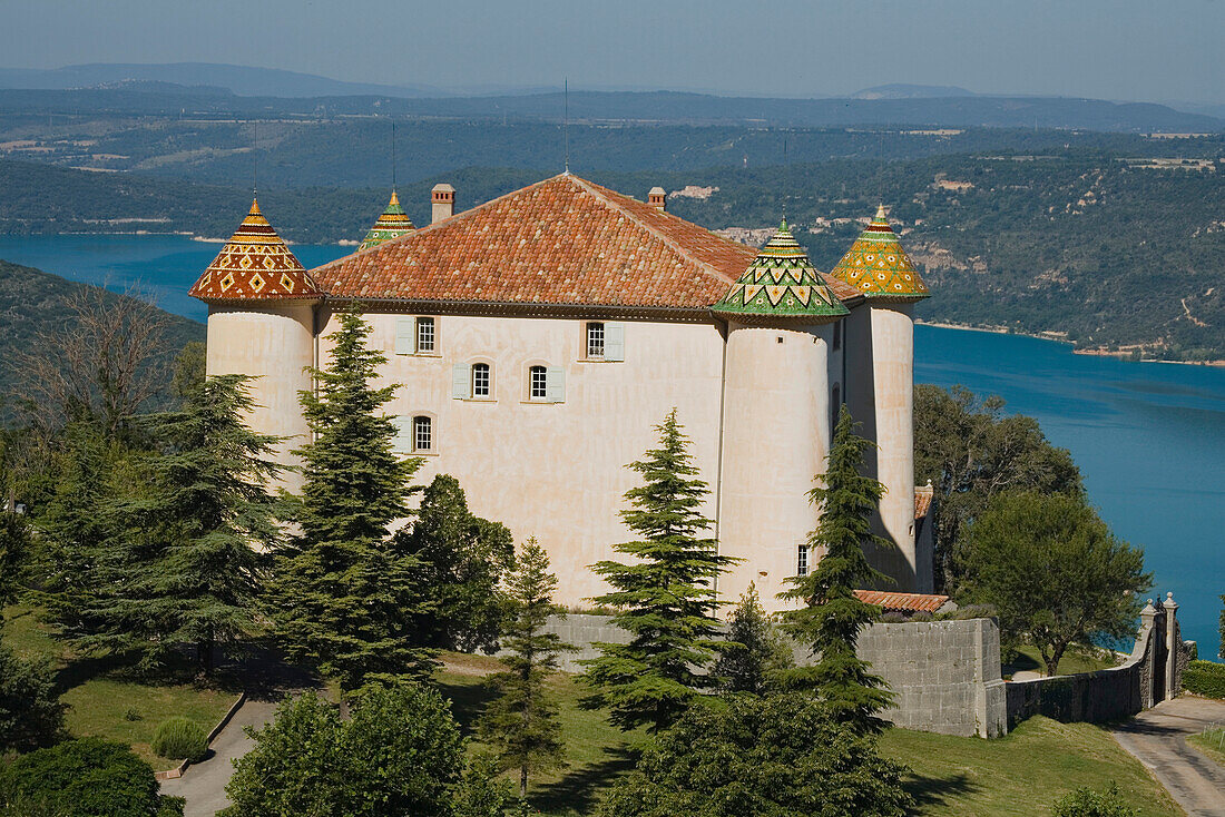 The castle of Aiguines with its coloured roof tiles in front of the lake Lac de Ste. Croix, Var, Provence, France