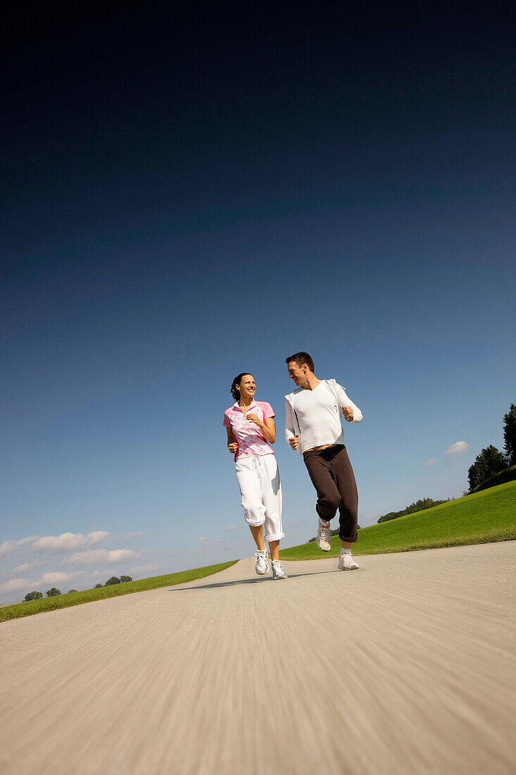 Paar joggt über Landstraße, Münsing, Bayern, Deutschland