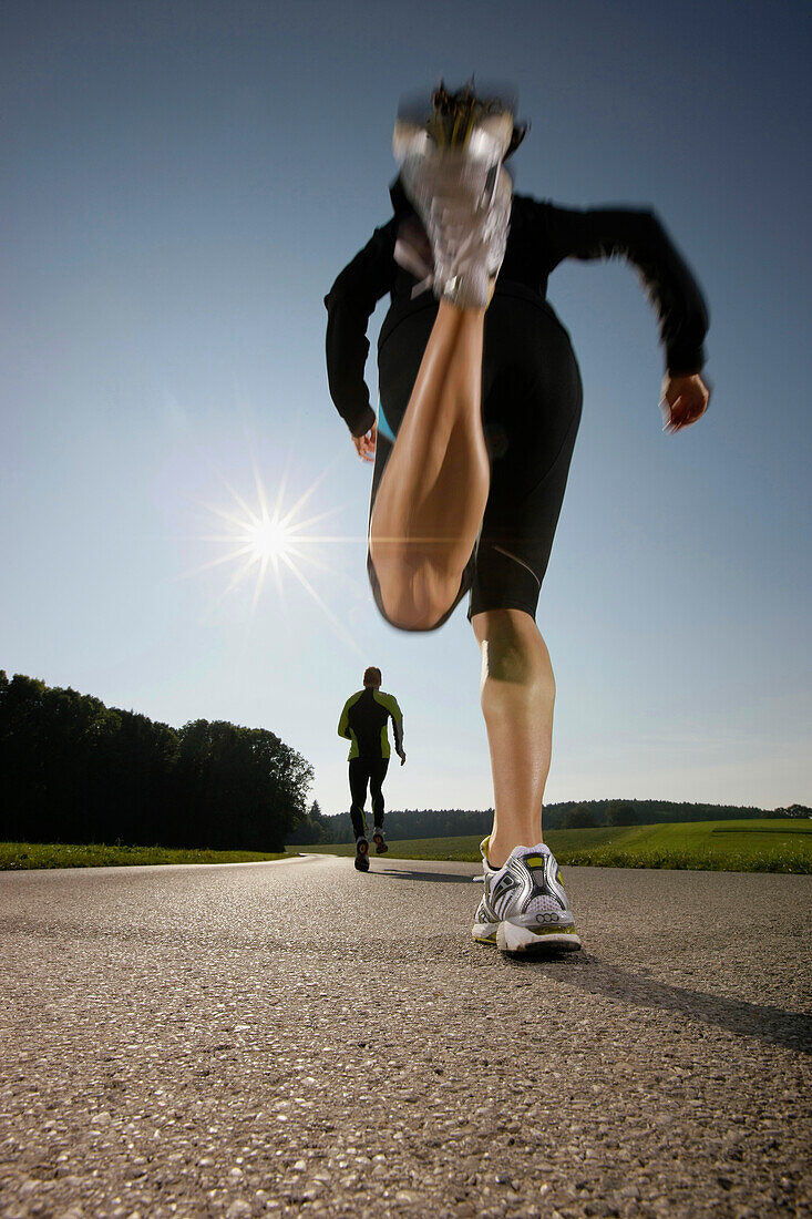 Two persons jogging along road, Strasslach-Dingharting, Bavaria, Germany