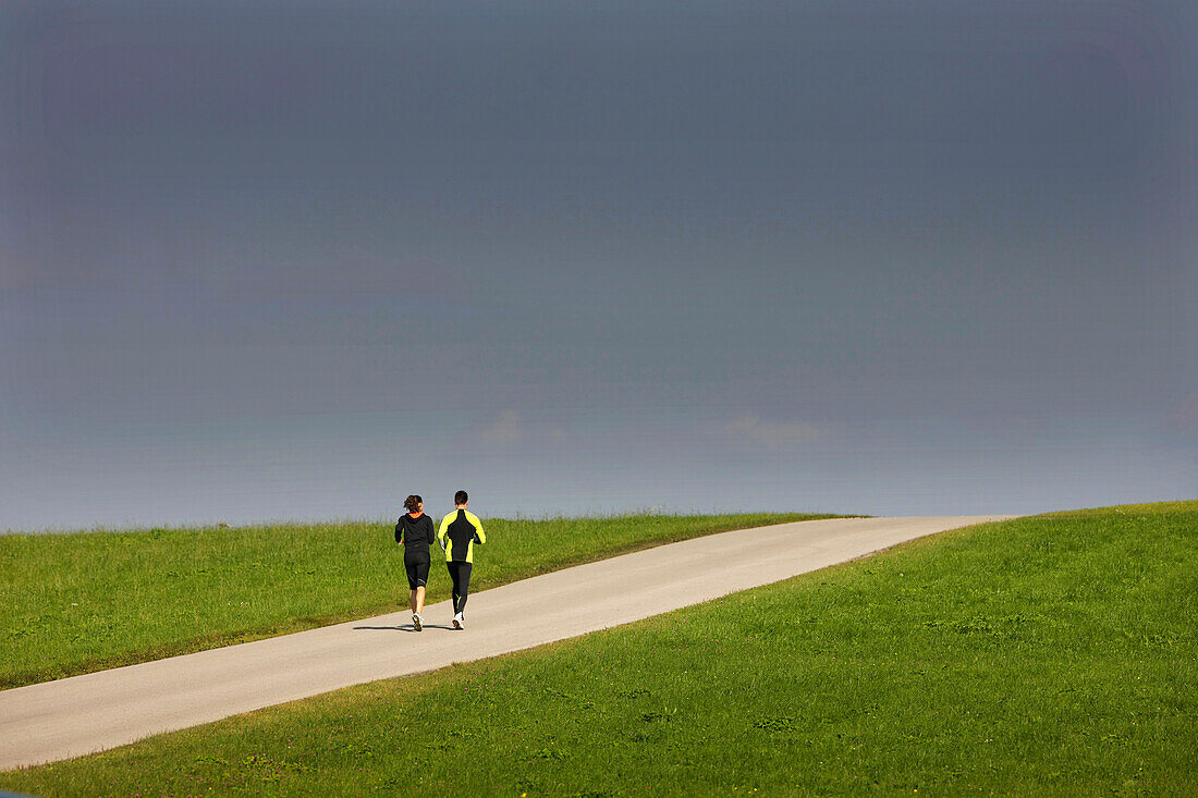 Paar joggt über Landstraße, Münsing, Bayern, Deutschland