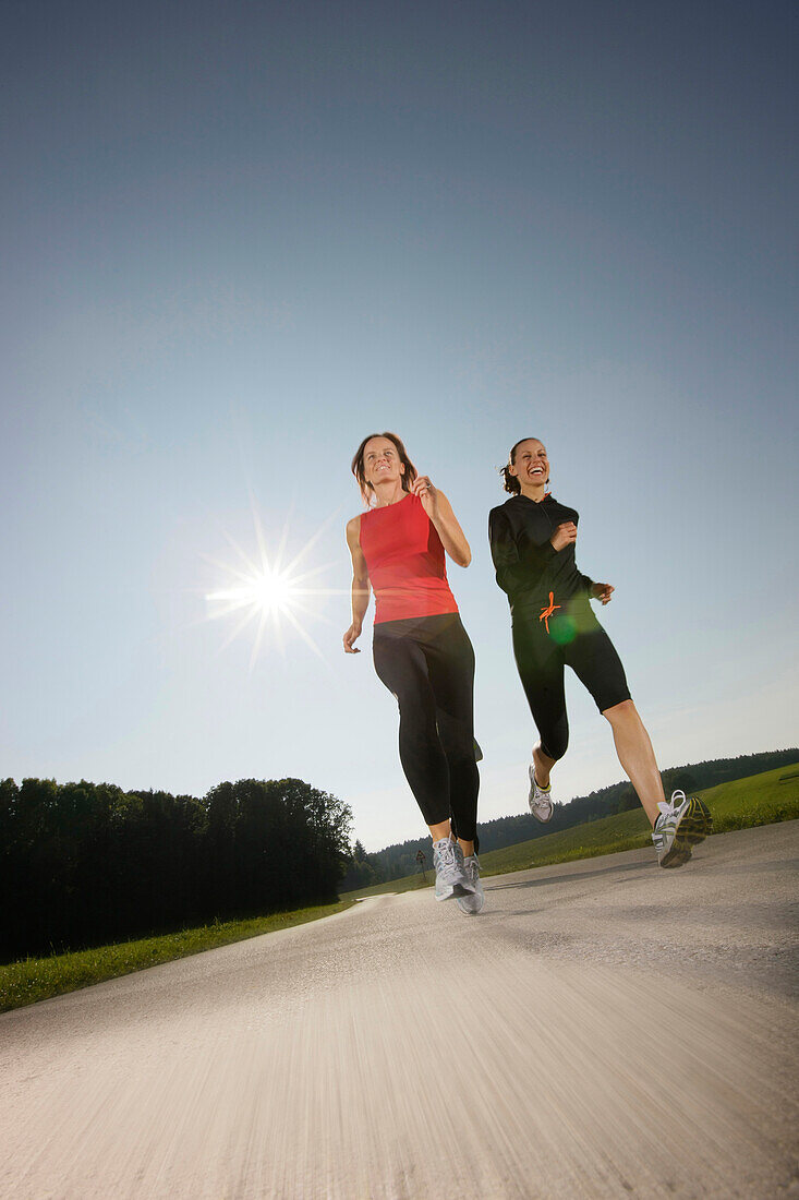 Two women running along road, Strasslach-Dingharting, Bavaria, Germany