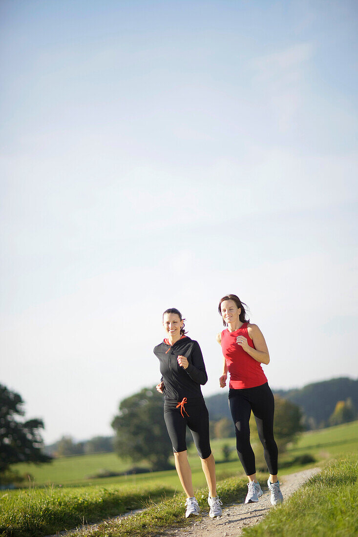 Two women running along dirt road, Munsing, Bavaria, Germany