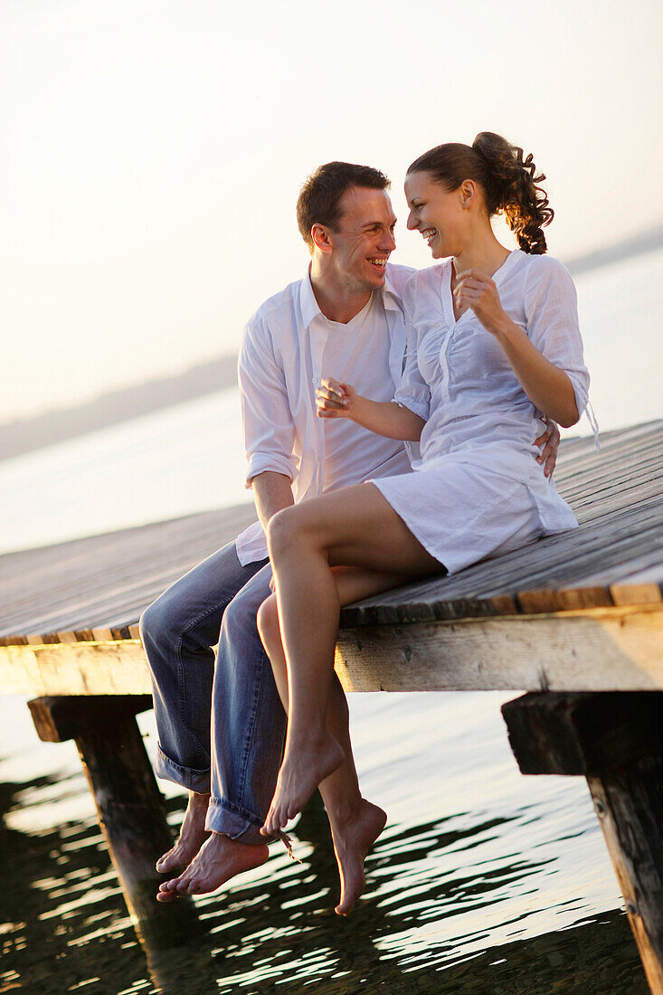 Couple sitting on a jetty, Ambach, Lake Starnberg, Bavaria, Germany