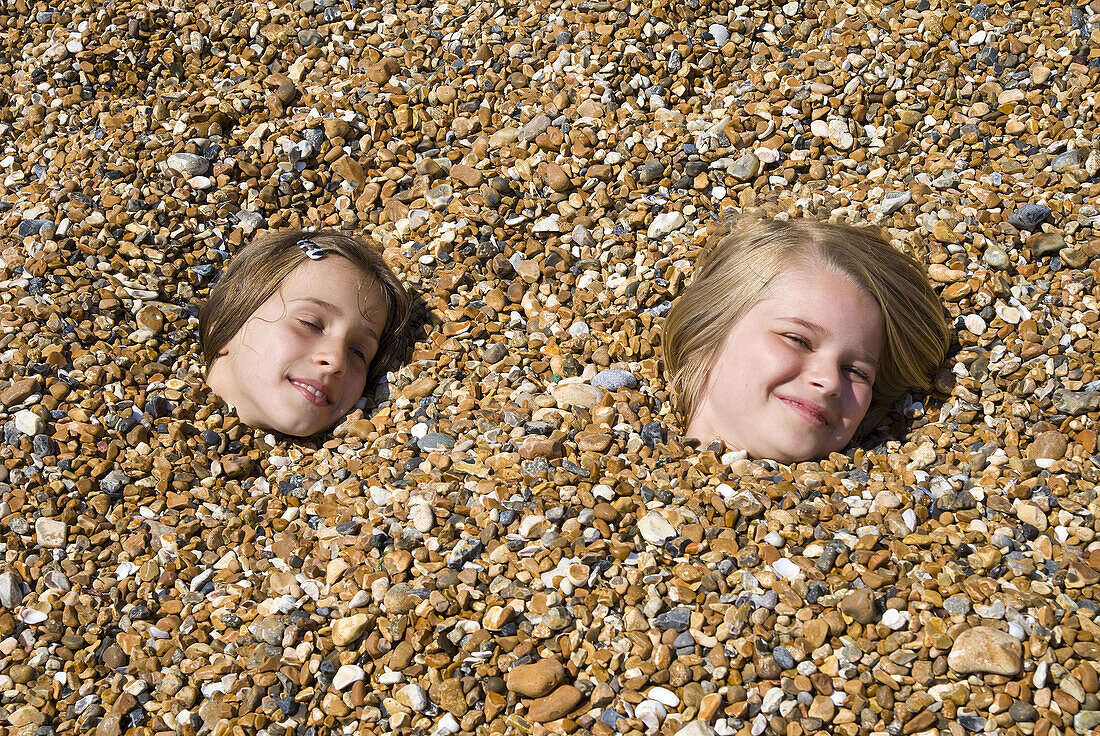 Children buried on pebbly beach, Brighton, England, UK