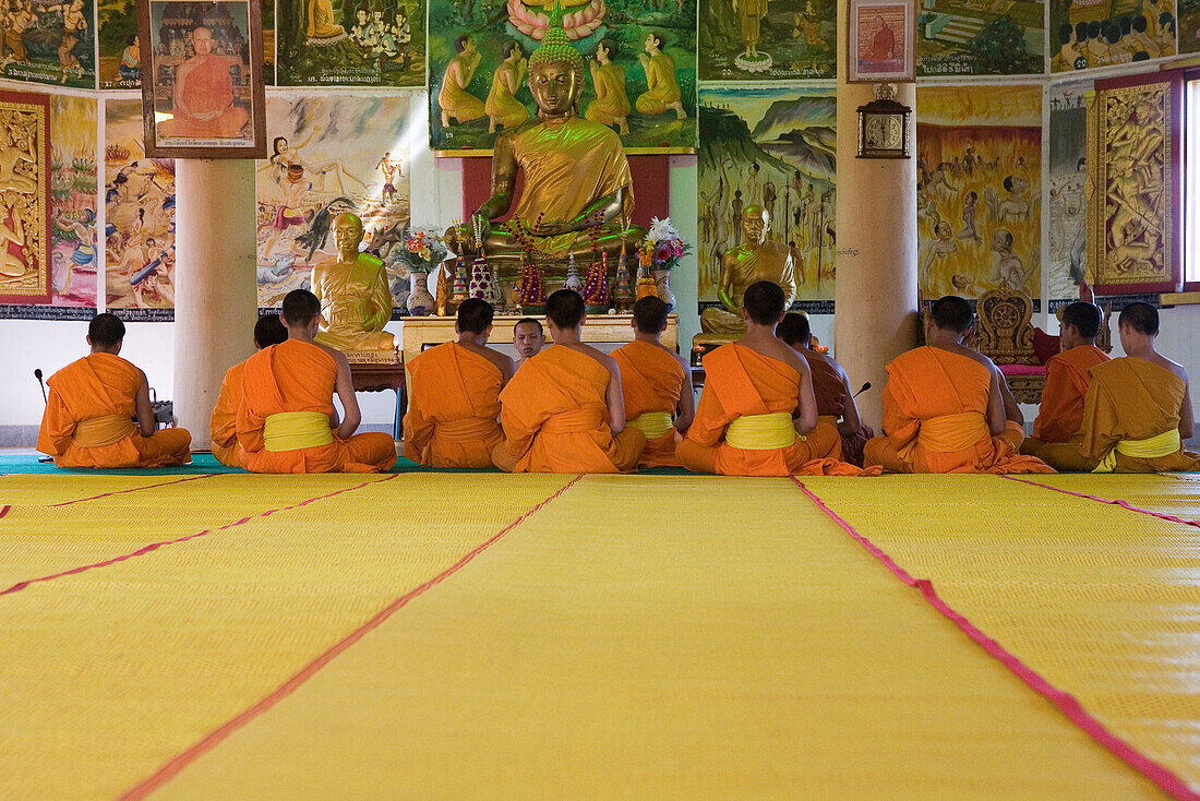 Buddhistische Mönche sitzen vor einer Buddhastatue im Kloster Vat Pa Phonphao, Luang Prabang, Laos