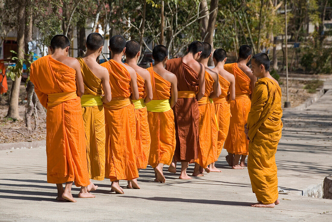 Buddhistic monks walking on a street in front of the monastery Vat Pa Phonphao, Luang Prabang, Laos