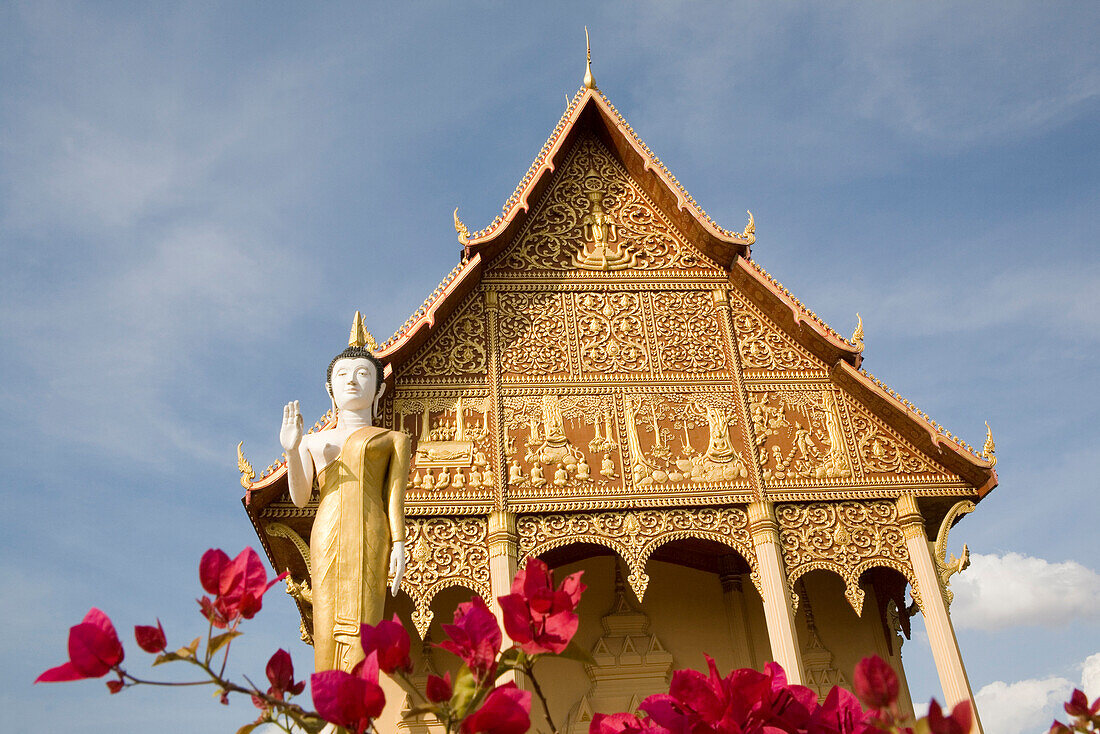Rote Blüten vor Statue und Tempel, Vat That Luang Neua, Vientiane, Provinz Vientiane, Laos
