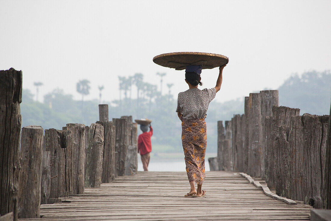 Zwei burmesische Frauen von hinten tragen einen Korb auf dem Kopf auf der U Bein Brücke in Amarapura bei Mandalay, Myanmar, Burma
