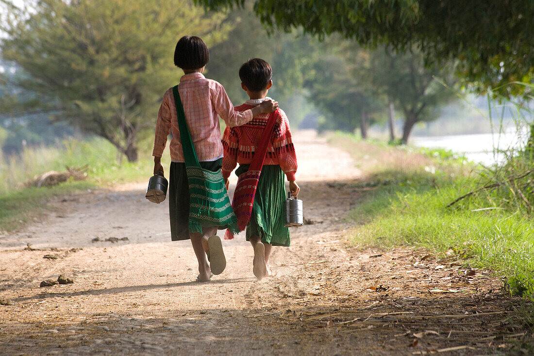 Two young school girls from behind walking on Inwa island ( Ava ) at Ayeyarwady River near Amarapura, Myanmar, Burma