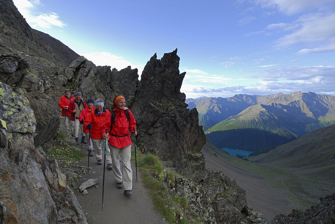 Group of hikers descending from alpine lodge Similaunhuette to reservoir Vernagtsee, Oetztal range, South Tyrol, Italy