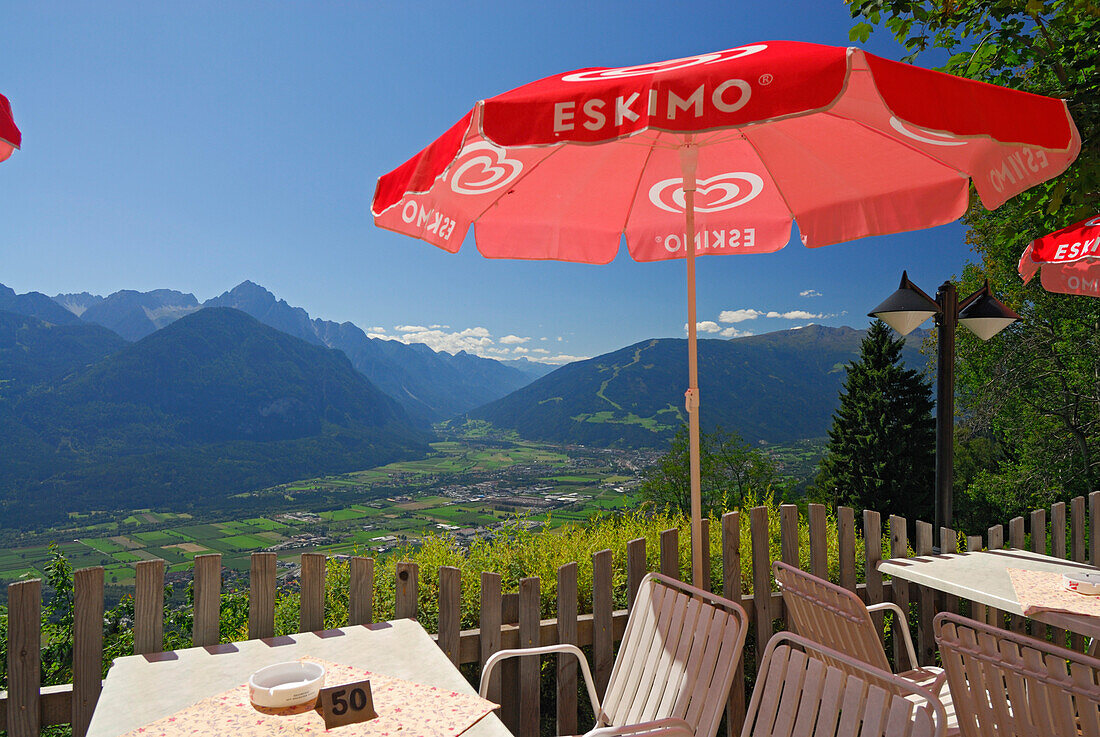 table and seats under red sunshade with view to valley of Lienz and Lienzer Dolomites range, Schobergruppe range, Hohe Tauern range, East Tyrol, Austria