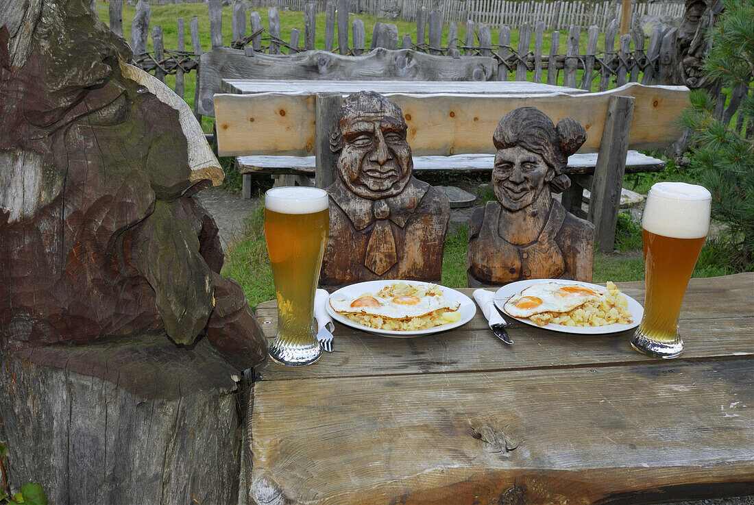 Holzfiguren an einem Tisch mit Essen und Weißbier, Sulzenaualm, Stubaier Alpen, Stubai, Tirol, Österreich