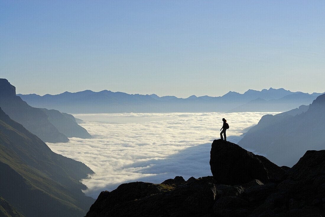 Hiker standing on crag above fog bank in valley Gschnitz, Stubai Alps, Stubai, Tyrol, Austria