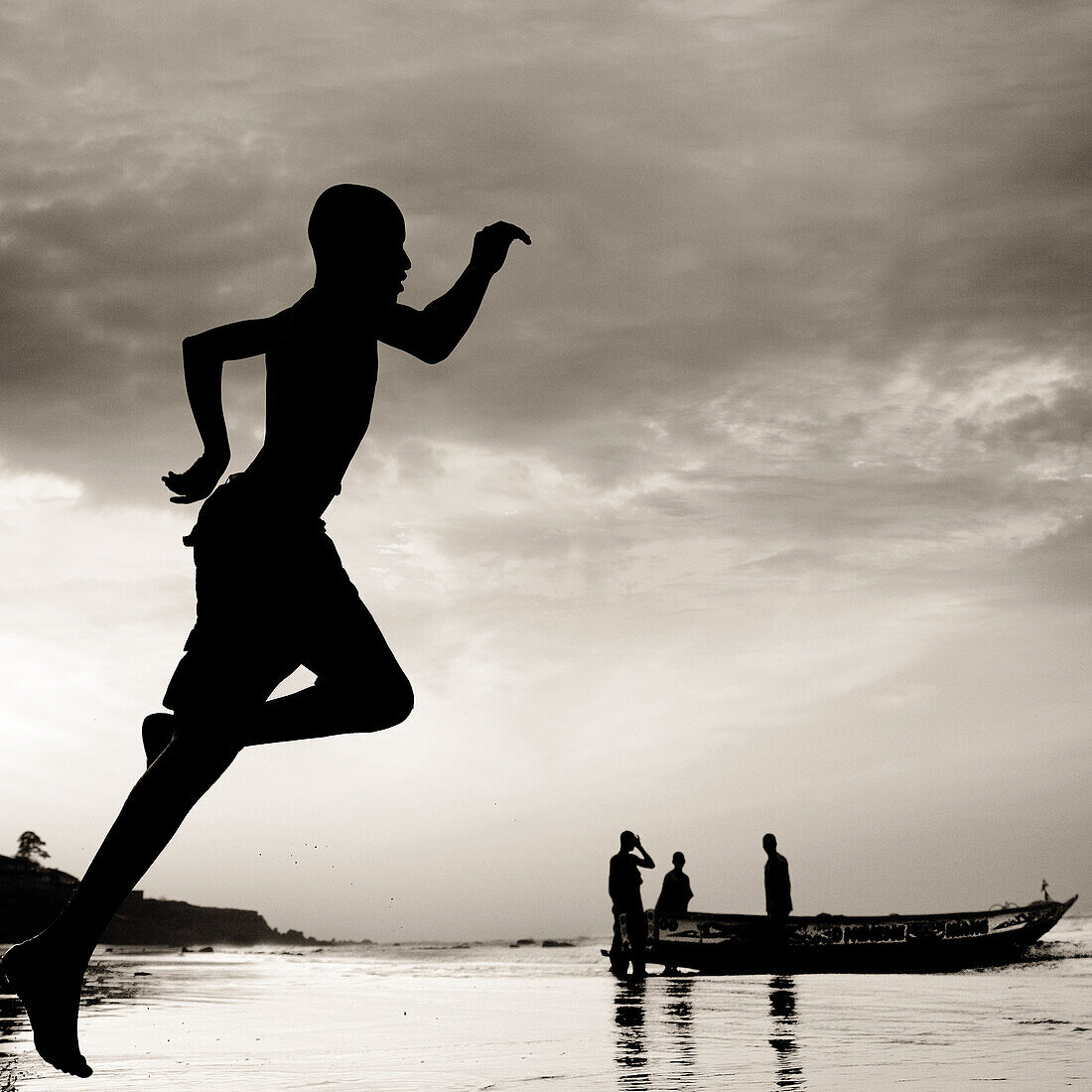 Young boy running on beach and fishermen in background. Gambia