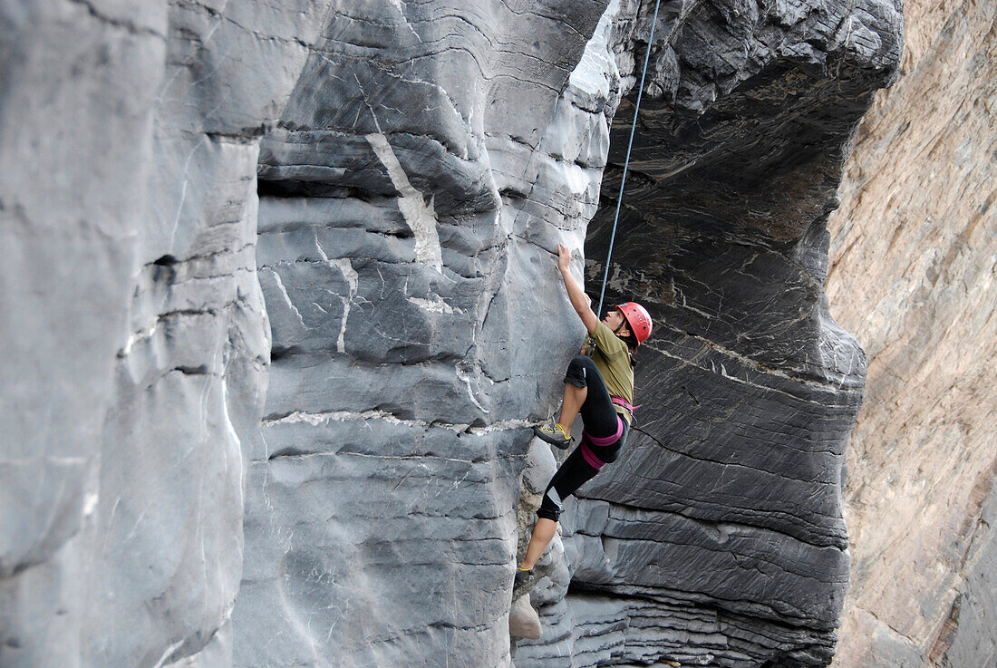 A man climbing up a rock face, Al Hajar mountains, Oman, Asia