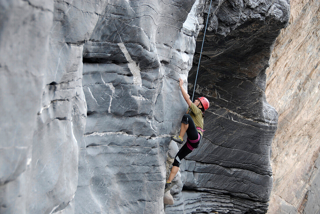 Ein Mann klettert eine Felswand hinauf, Al Hajar Berge, Oman, Asien