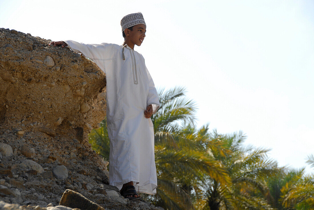 A boy standing on a stony embankment, Al Hajar mountains, Wadi, Oman, Asia