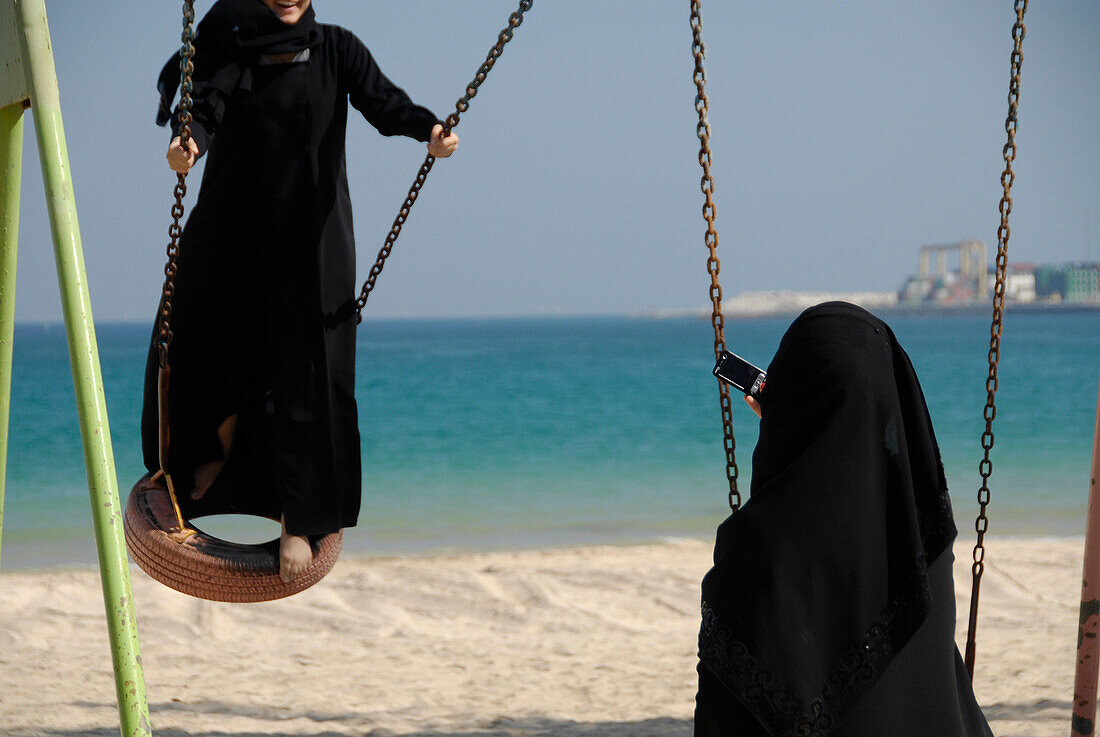 Zwei einheimische Mädchen auf einer Schaukel am Strand, Al Fujairah, Vereinigte Arabische Emirate