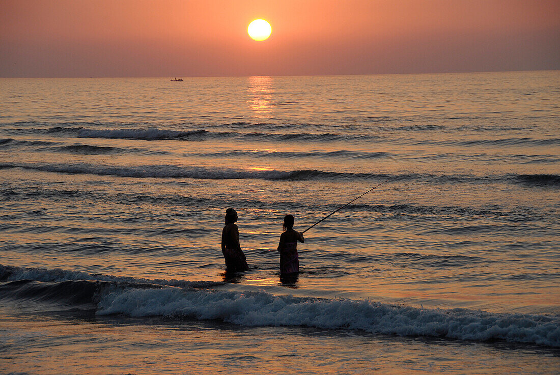 Zwei Menschen stehen bei Sonnenuntergang im Meer und angeln, Musandam, Oman, Asien