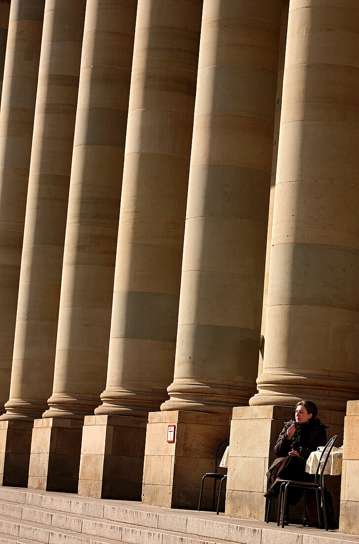 Woman sitting between the columns of the Koenigsbau in the sunlight, Stuttgart, Baden-Wuerttemberg, Germany