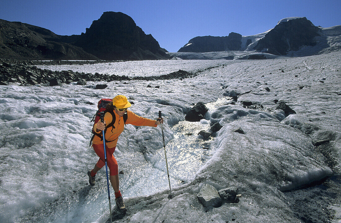 Woman crossing stream on Pers glacier, Piz Trovat and Piz Cambrena in background, Upper Engadin, Engadin, Grisons, Switzerland