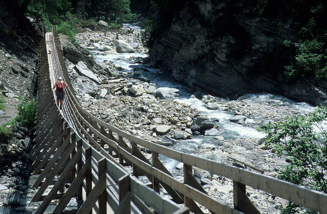 Woman with backpack on suspension bridge high up in valley Val Sinestra, Silvretta, Silvretta range, Unterengadin, Engadin, Grisons, Switzerland