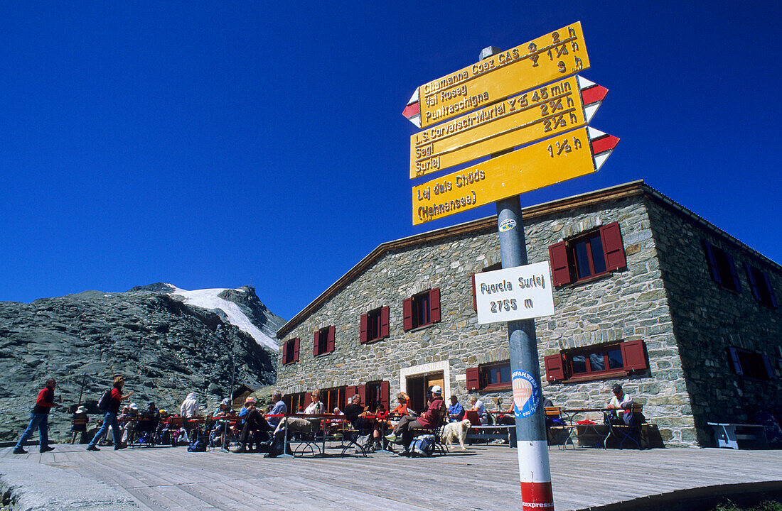 Gelber Schweizer Wanderwegweiser vor der Terrasse der Fuorcla Surlej-Hütte mit vielen Wanderern bei der Rast, Fuorcla Surlej, Berninagruppe, Bernina, Oberengadin, Engadin, Graubünden, Schweiz