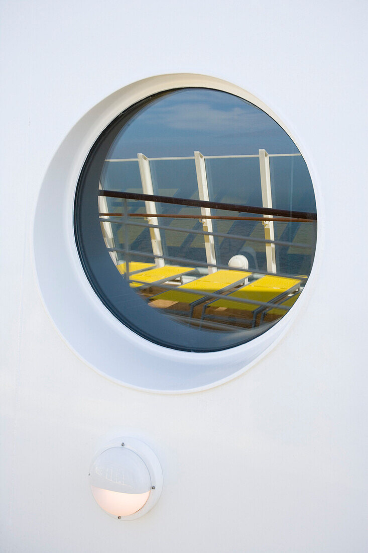 Porthole of cruise ship AidaDiva reflecting sunloungers