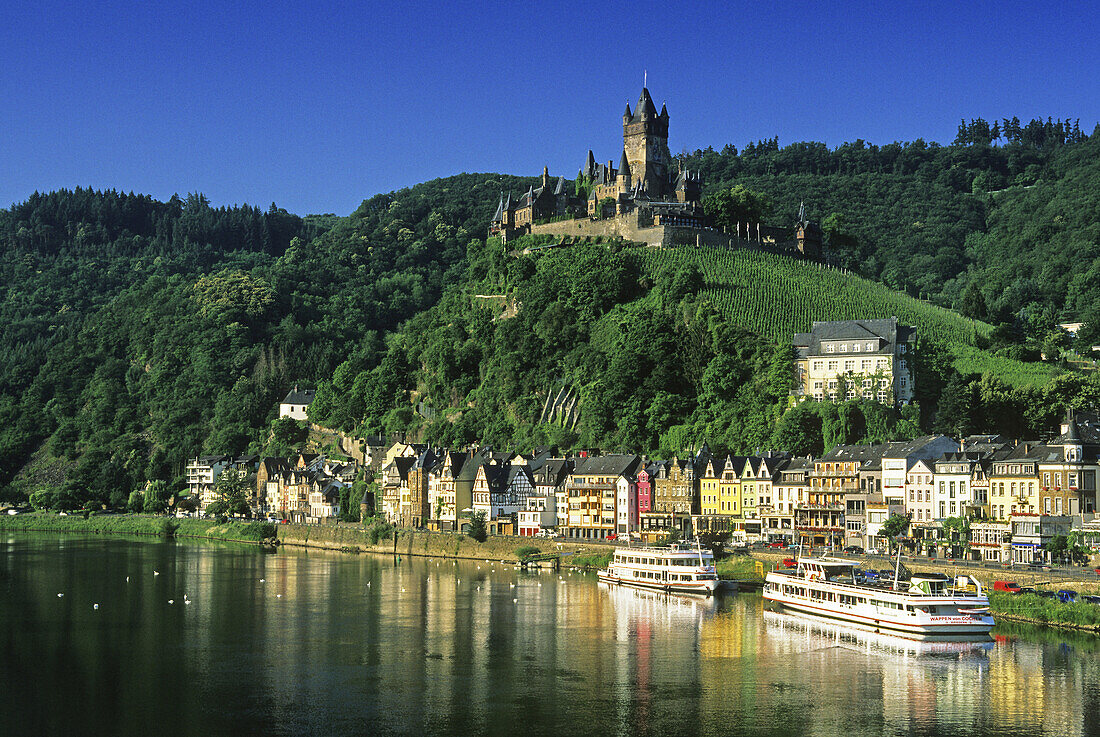 Reichsburg unter blauem Himmel und Ausflugsschiffe am Ufer, Mosel, Rheinland-Pfalz, Deutschland