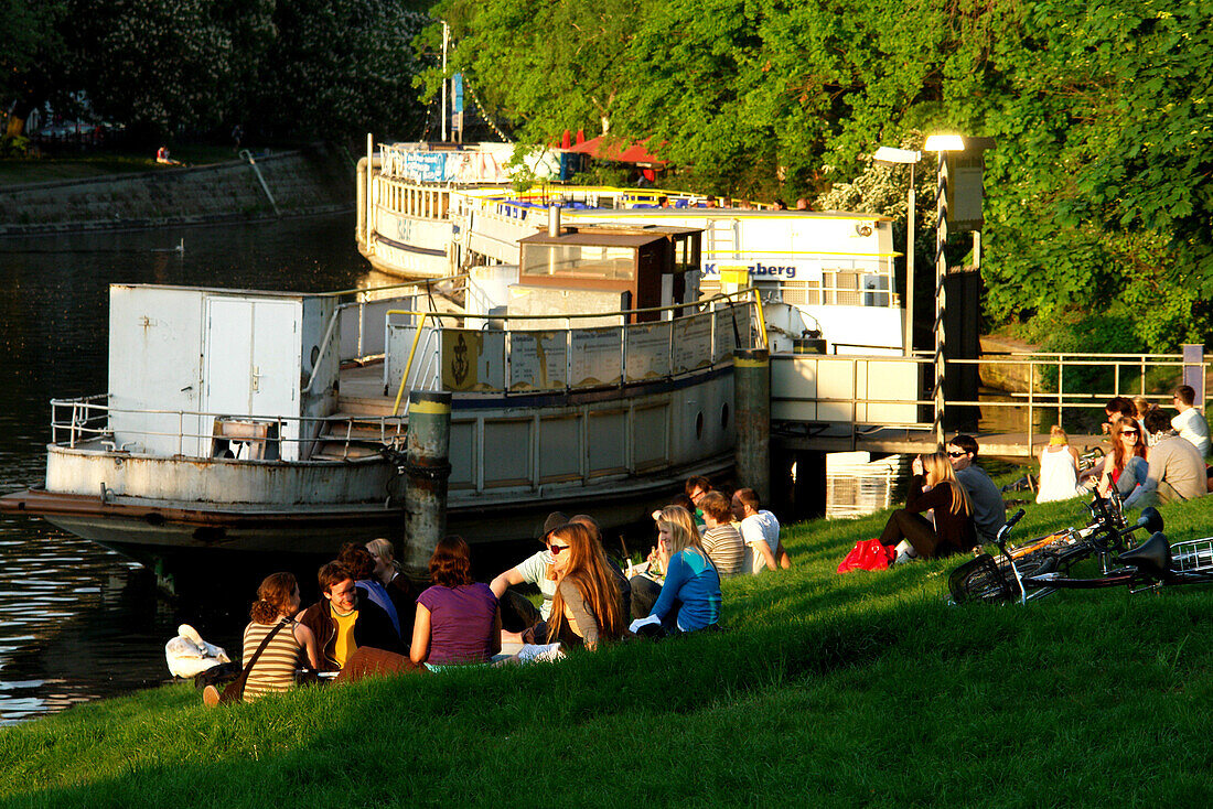 Young people sitting along the banks of a canal, Berlin, Germany
