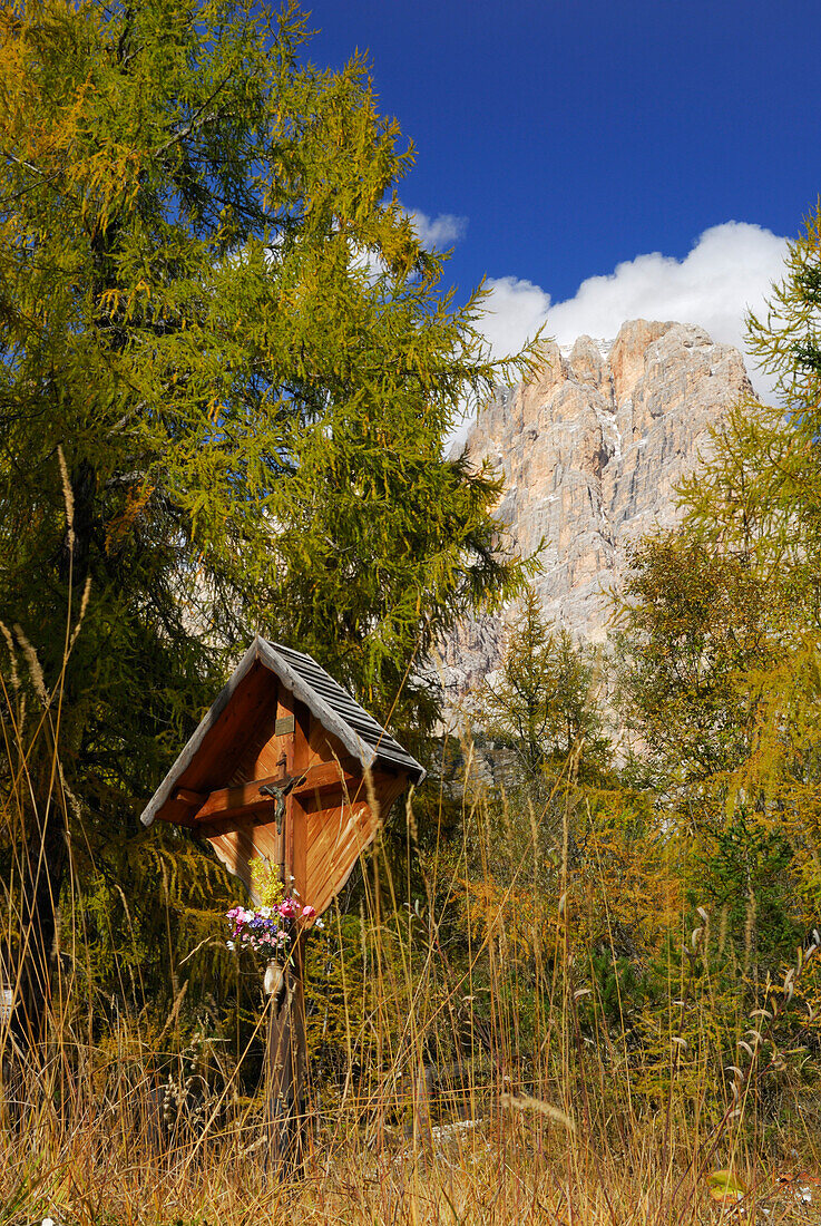 Cross beneat Cristallo range with larches in autumn colours, Dolomites, South Tyrol, Italy