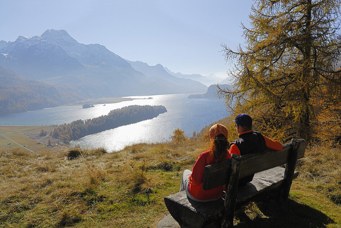 Couple sitting on bench above lake Sils, Piz da la Margna in background, Upper Engadin, Engadin, Grisons, Switzerland