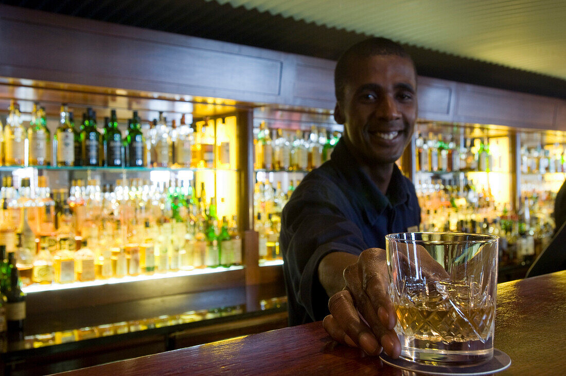 Smiling barkeeper serving a glass of whiskey, Bascule Bar, Cape Grace Hotel, Cape Town, South Africa, Africa