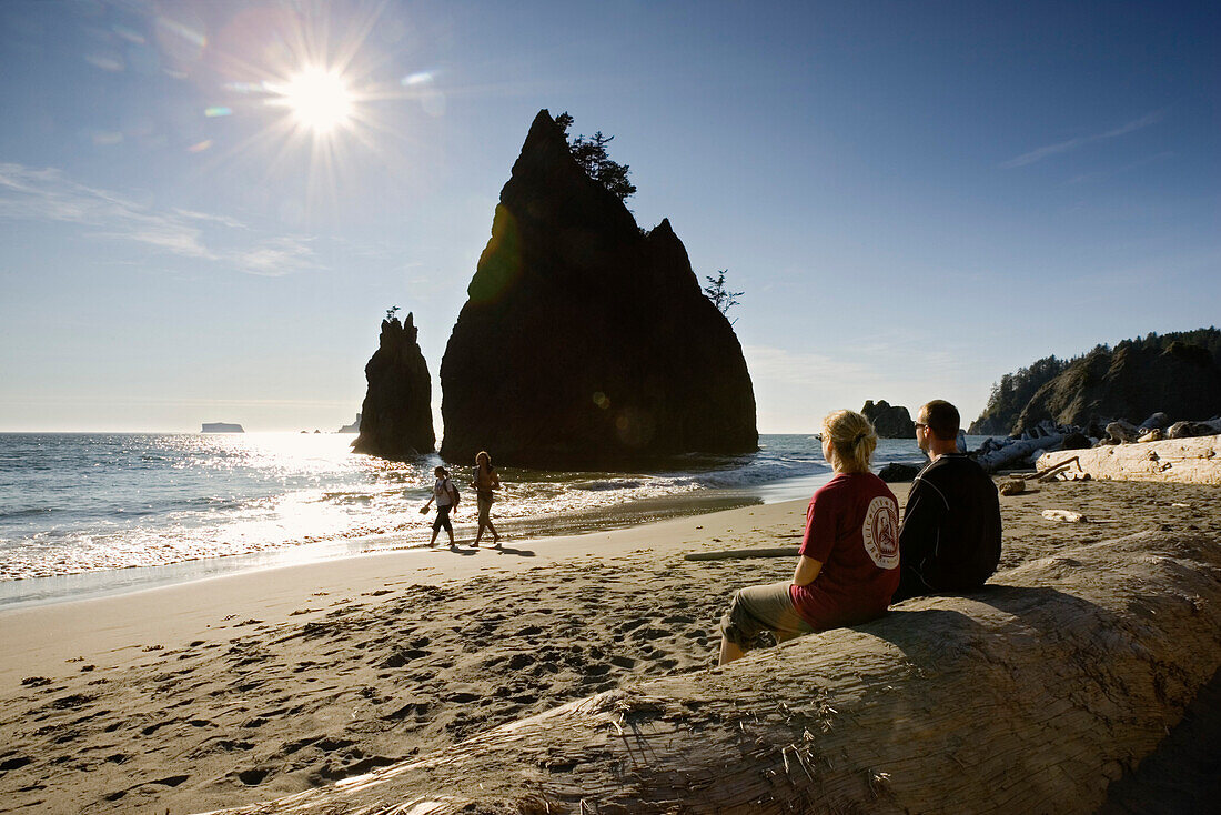 A couple sitting on driftwood at Rialto Beach, Olympic Peninsula, Washington, USA