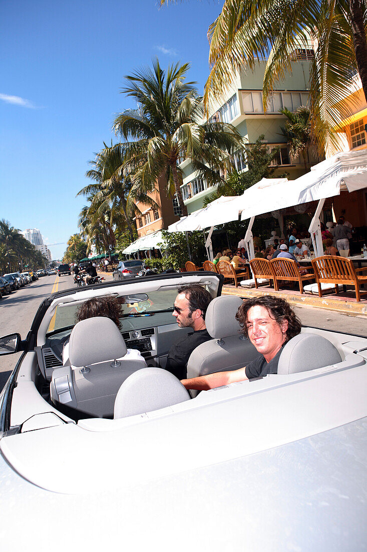 Drei Männer fahren in einem Cabriolet auf dem Ocean Drive, South Beach, Miami Beach, Florida, USA