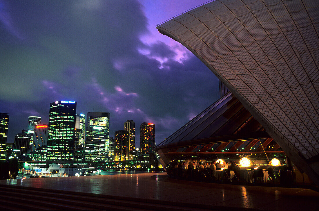 Menschen im Bennelong Restaurant im Opernhaus und beleuchtete Hochhäuser, Sydney, New South Wales, Australien