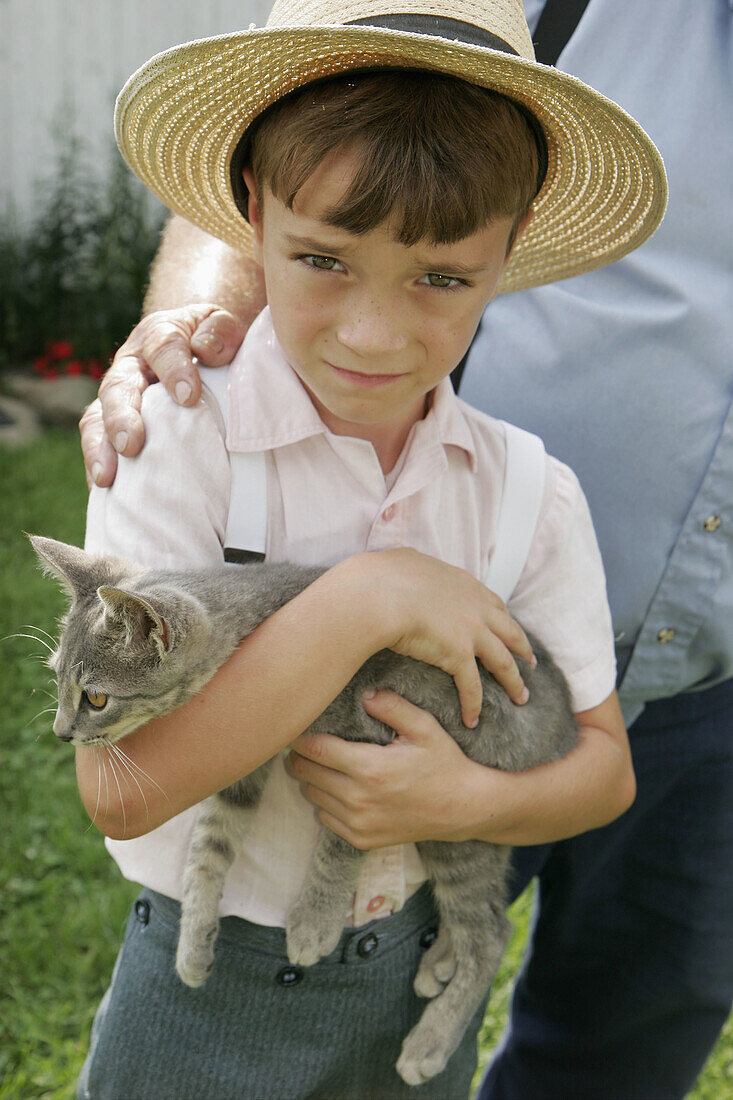 Amish Farm Tour, boy, kitten, straw hat. Shipshewana. Indiana. USA.
