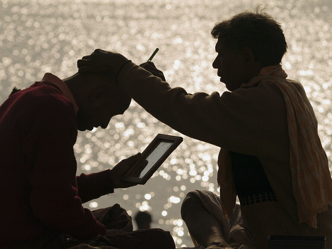 A barber shaves a man's head with a straight razor in the early morning sun on the banks of the Ganga river in Varanasi, India