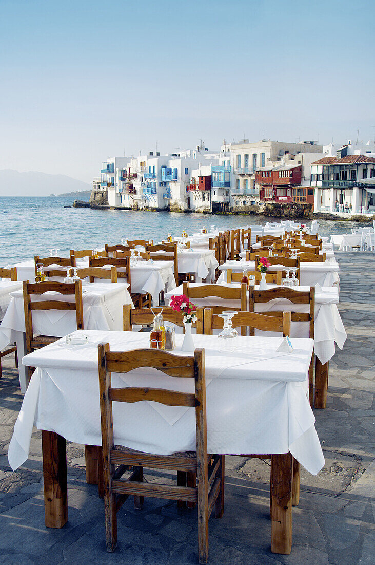 Restaurants with table and chairs in the Little Venice area overlooking the Aegean Sea in Hora on the Greek Island of Mykonos, Greece.
