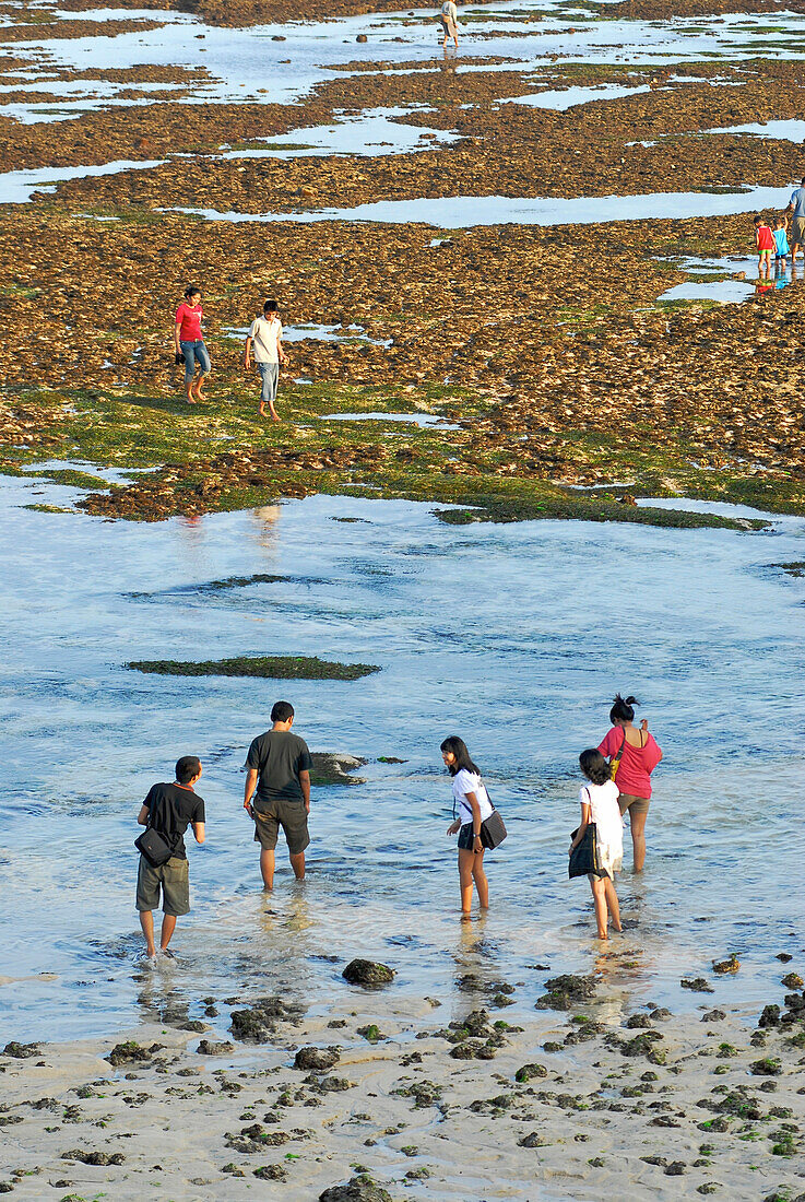 Balinese people strolling on the beach at low tide, Pura Geger, Southern Bali, Indonesia, Asia