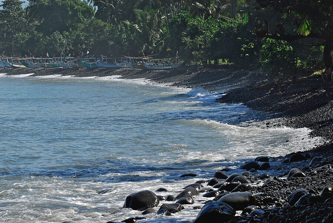 Stony beach with fishing boats in the background, Medewi, West Bali, Indonesia