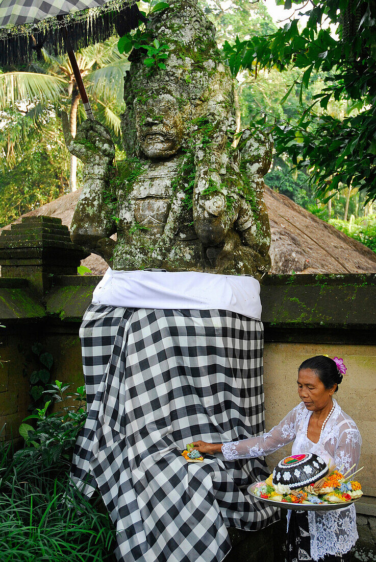 Ältere Frau mit Opfergabe vor einer Steinfigur, Amandari Hotel, Yeh Agung, Bali, Indonesien, Asien