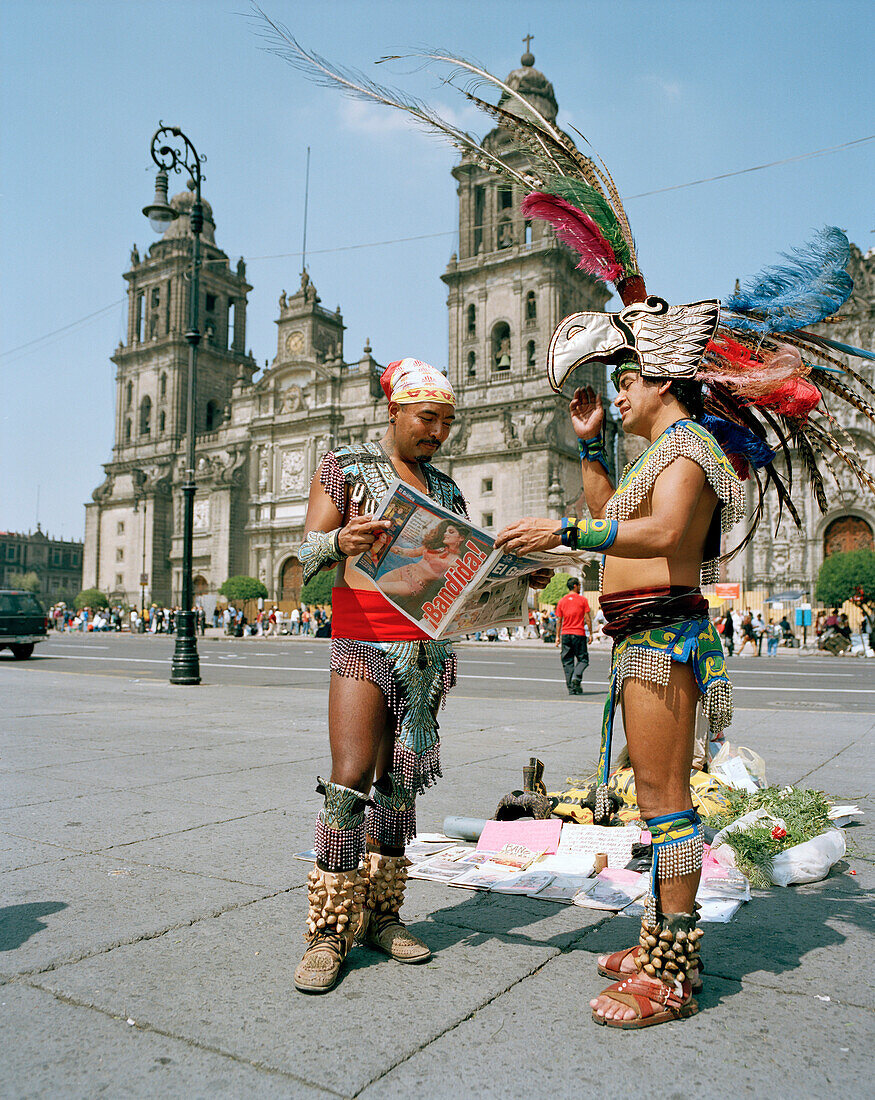 Men wearing aztec costumes reading a newspaper at the Zocalo in front of the cathedral, Mexico City, Mexico, America