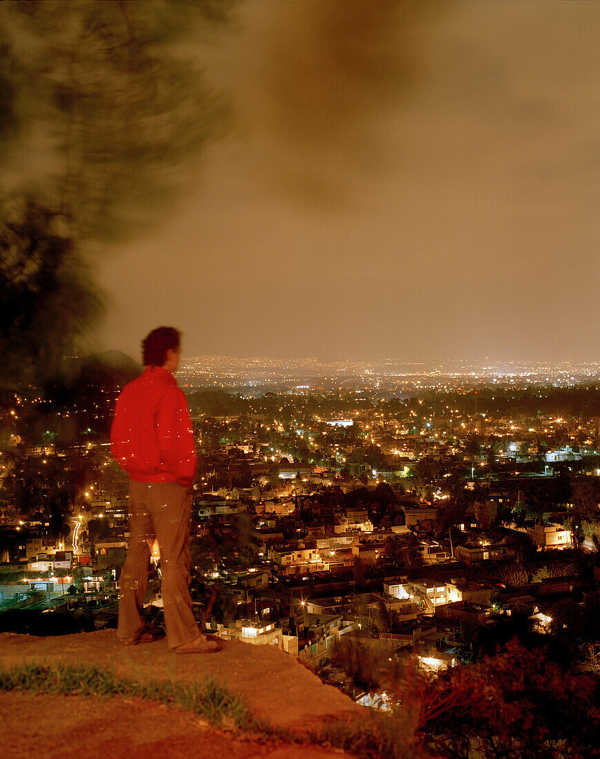 A man looking from Barrio Xochimilco at the lights of Mexico City, Mexico, America