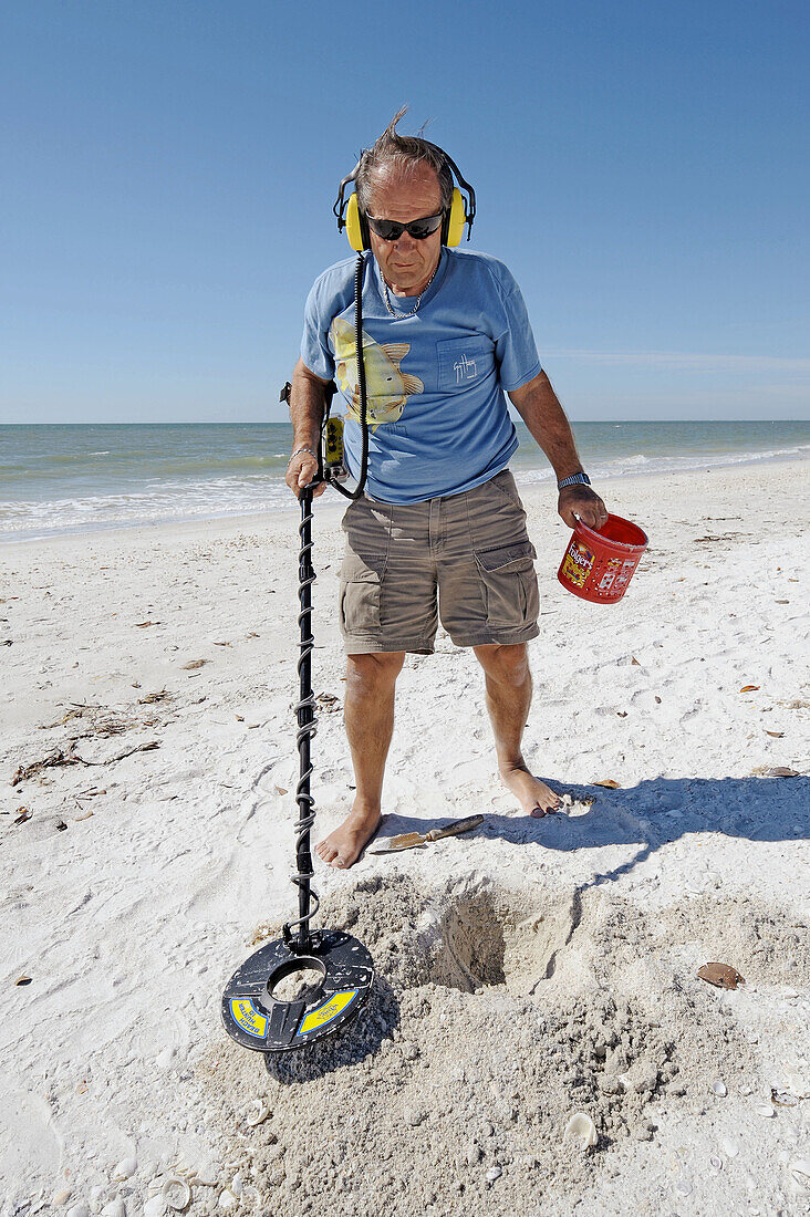 Senior male uses metal detector to find objects on a beach at Naples Florida
