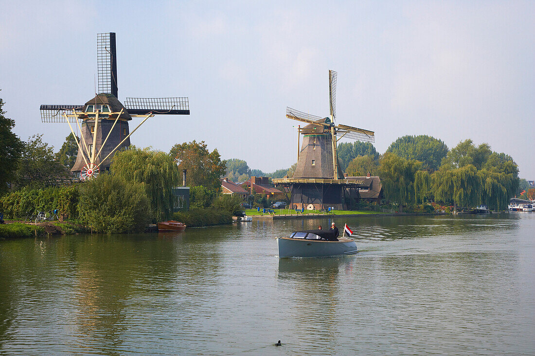 Ein Motorboot fährt auf dem Fluss Vecht an zwei Windmühlen vorbei, Weesp, Niederlande, Europa